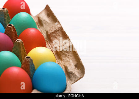 Multi-colored Easter eggs in a box on a white table. Copy space Stock Photo