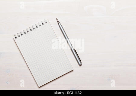 Open blank notepad with spiral and gray pen on white wooden background. Top view. Copy space Stock Photo