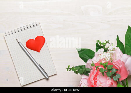 Opened blank notepad with spiral, gray pen, heart and pink peony flowers on white wooden background. Top view. Copy space. Stock Photo