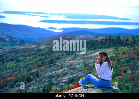 A young woman takes a photograph in Acadia National Park, Maine. On the top of Cadilac Mountain. Stock Photo