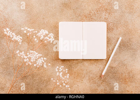Open notebook with white pencil among white flower plant. Flat lay, top view, cmock up. The concept of planning and goals to set on New Year. Stock Photo