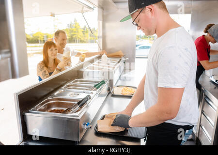 Young chefs in a food truck preparing food for their waiting customers Stock Photo