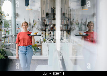 Portrait of young woman serving coffee and cake in a cafe Stock Photo