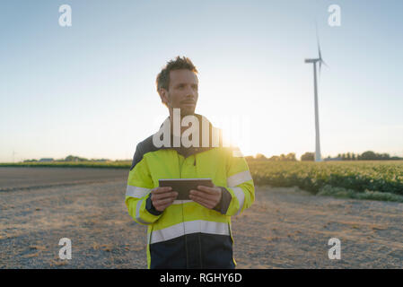 Engineer standing in rural landscape at a wind turbine holding tablet Stock Photo