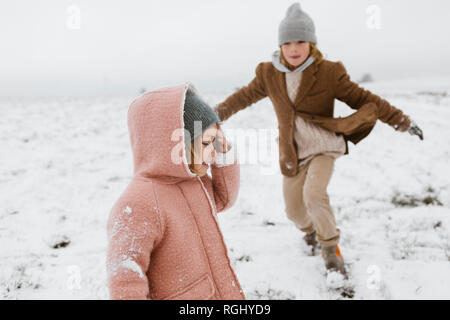 Happy little girl in the snow with brother playing in the background Stock Photo
