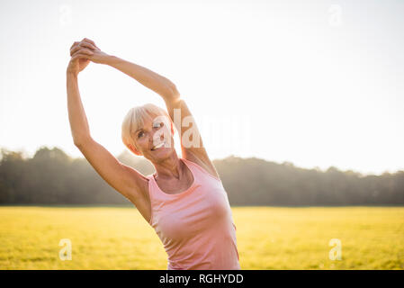 Senior woman stretching on rural meadow at sunset Stock Photo
