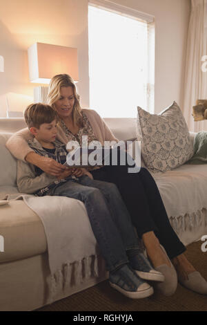 Side view of attractive mother with her son spending time together while reading story book in living room at home Stock Photo