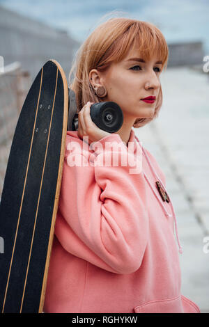 Cool young woman holding carver skateboard outdoors Stock Photo