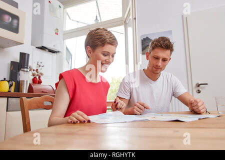 Smiling young couple sitting at table at home with map Stock Photo