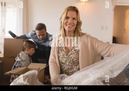 Portrait of happy mother smiling with her family in the background unpacking cardboard boxes in their new home Stock Photo