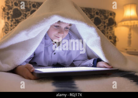 Boy under blanket using digital tablet in bedroom at home Stock Photo
