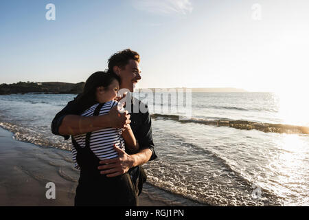 France, Brittany, happy young couple hugging on the beach at sunset Stock Photo
