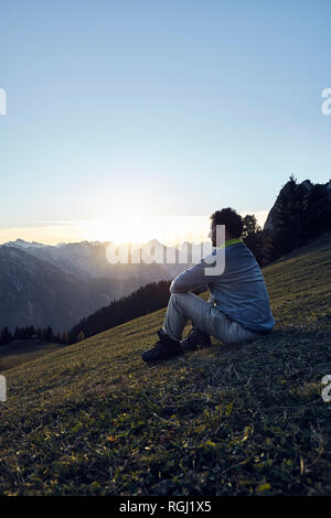 Austria, Tyrol, Rofan Mountains, hiker sitting on meadow at sunset Stock Photo