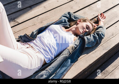 Relaxed young woman lying on wooden boards in sunshine Stock Photo