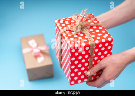 Women's hands holding gift box Packed in red polka dot paper on blue background. Concept holiday card for Valentine's day and women's day Stock Photo