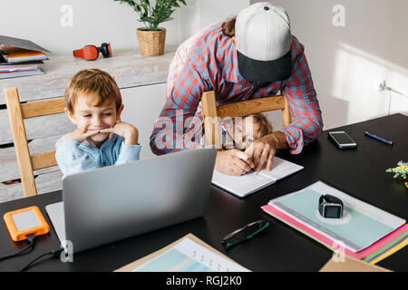 Father writing in notebook while children are playing at his desk Stock Photo