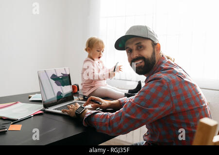 Father working from home, using laptop with his gaughter sitting on the desk, playing Stock Photo