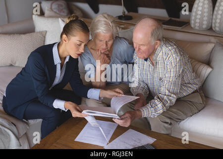 Front view of a female doctor and senior couple looking and discussing over medical reports they hold in their hands at home Stock Photo