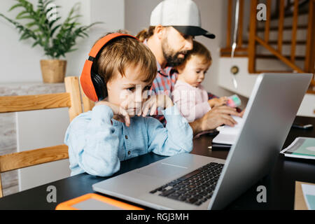 Father working at home, using laptop with his children on his lap Stock Photo