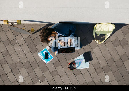 Young businessman sitting outdoors at a wall working on laptop Stock Photo