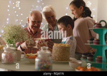 Multi-generation family giving present to birthday boy at home, sitting at a table with sweet food Stock Photo