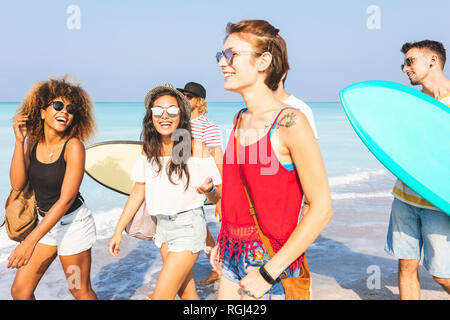 Group of friends walking on the beach, carrying surfboards Stock Photo