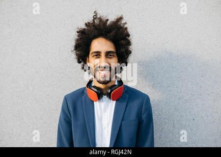 Portrait of smiling young businessman with headphones at a wall Stock Photo