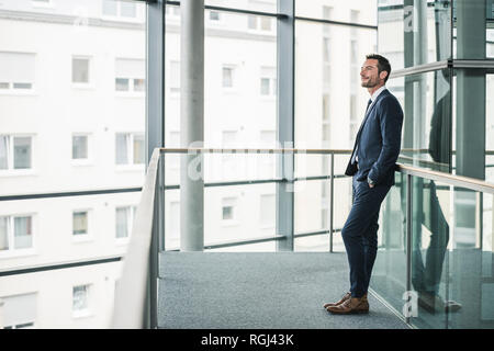 Successful businessman standing in office building, looking out of window, daydreaming Stock Photo