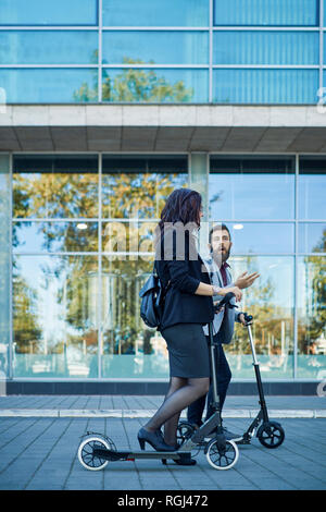 Businessman and businesswoman with scooters talking on pavement Stock Photo
