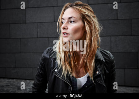 Confident young woman wearing biker jacket looking away