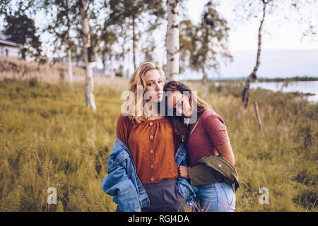 Two girl friends leaning on each other on a lakeshore Stock Photo