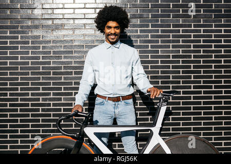 Mid adult man standing in front of black wall, holding his bicycle Stock Photo