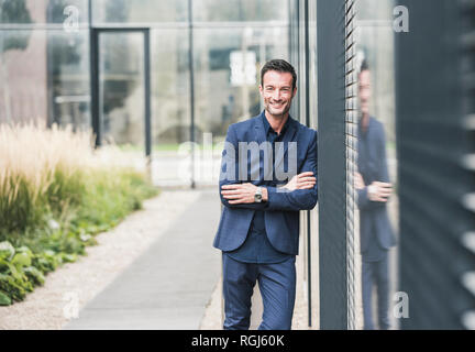 Portrait of a businessman leaning on a wall, smiling Stock Photo