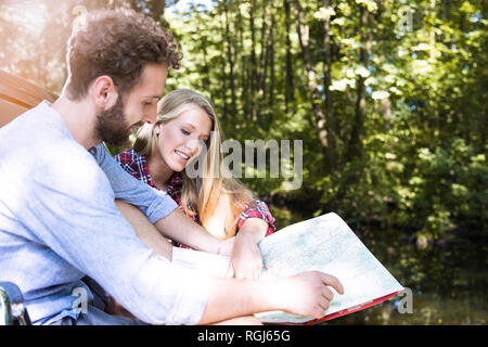 Smiling young couple reading map at a brook Stock Photo