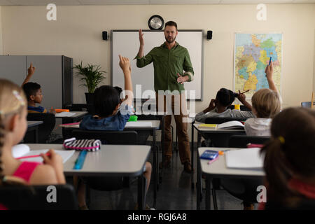 Front view of school teacher teaching to students who raised their hand in a classroom of elementary school Stock Photo