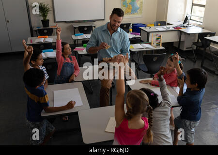 High angle view of school kids raising hands while teacher studying in classroom of elementary school Stock Photo