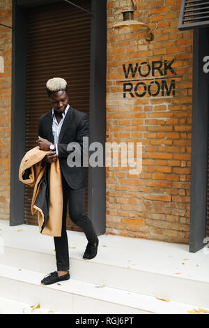 Handsome young Afro American businessman in classic suit smiling while leaving the office building Stock Photo