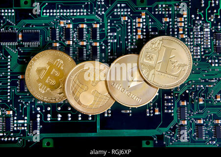 Litecoin, Ripple, Ethereum & Bitcoin gold coins representing cryptocurrenies against a computer circuit board. Stock Photo