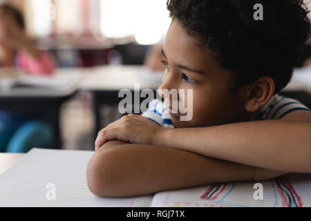 Close-up of thoughtful schoolboy leaning on desk and looking away in classroom Stock Photo