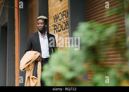 Handsome young Afro American businessman in classic suit smiling while leaving the office building Stock Photo