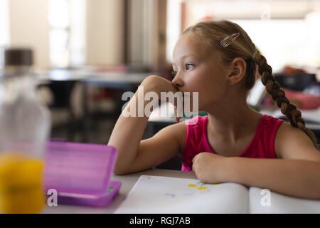 Close-up of thoughtful schoolgirl leaning on desk and looking away in classroom Stock Photo