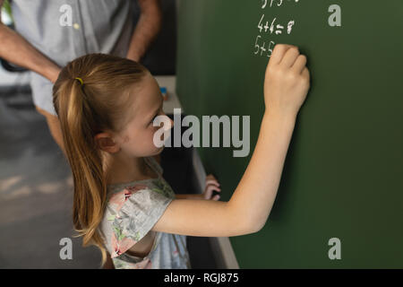 High angle view of schoolgirl writing on chalk board in classroom Stock Photo