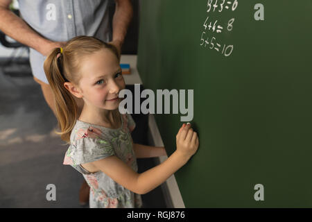 High angle view of schoolgirl writing on chalk board in classroom Stock Photo