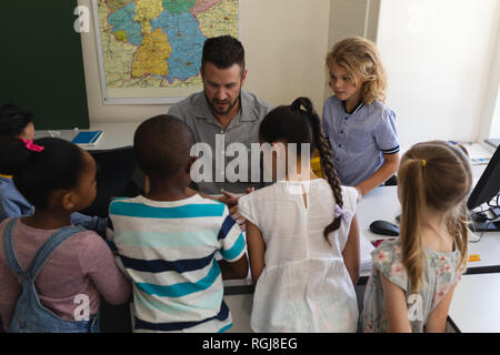 Male teacher assisting boys at desk in classroom Stock Photo - Alamy