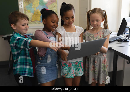 Front view of a group of happy and smiling schoolkids studying standing on digital tablet in classroom of elementary school Stock Photo