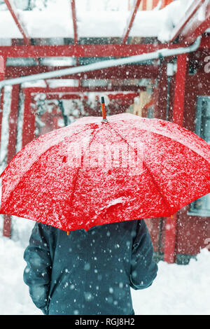 Sad and alone woman under red umbrella walking in winter snow through urban environment Stock Photo