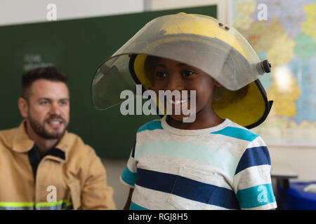 Happy schoolboy wearing fire helmet in classroom Stock Photo