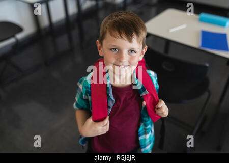 High angle view of happy schoolboy with schoolbag looking at camera in classroom Stock Photo