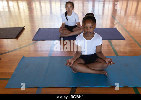 Schoolkids doing yoga and meditating on a yoga mat in school Stock Photo