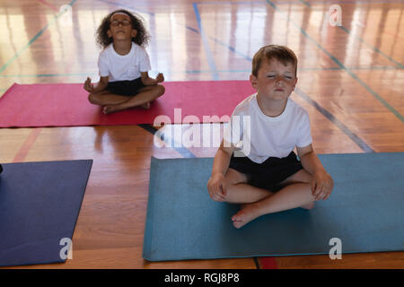 Schoolkids doing yoga and meditating on a yoga mat in school Stock Photo